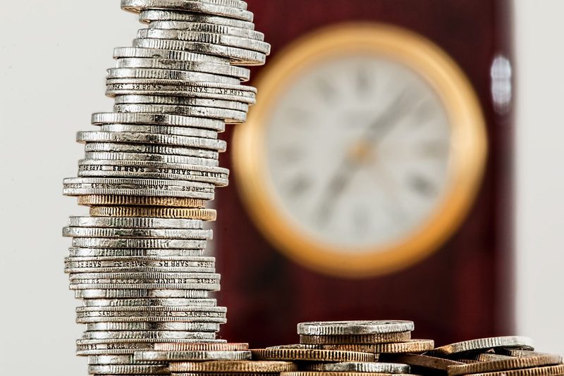 Stacked coins beside a clock, representing the deductible and premium trade-off